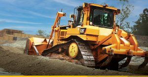 Cat dozer pushes dirt at a job site. The machine has steel undercarriage.
