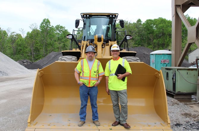 2 men posing in front of wheel loader bucket